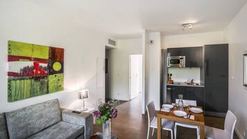 Ein modernes Wohnzimmer mit einem grauen Sofa, einem Esstisch für vier Personen und einer Küchenzeile mit Mikrowelle und Kühlschrank.