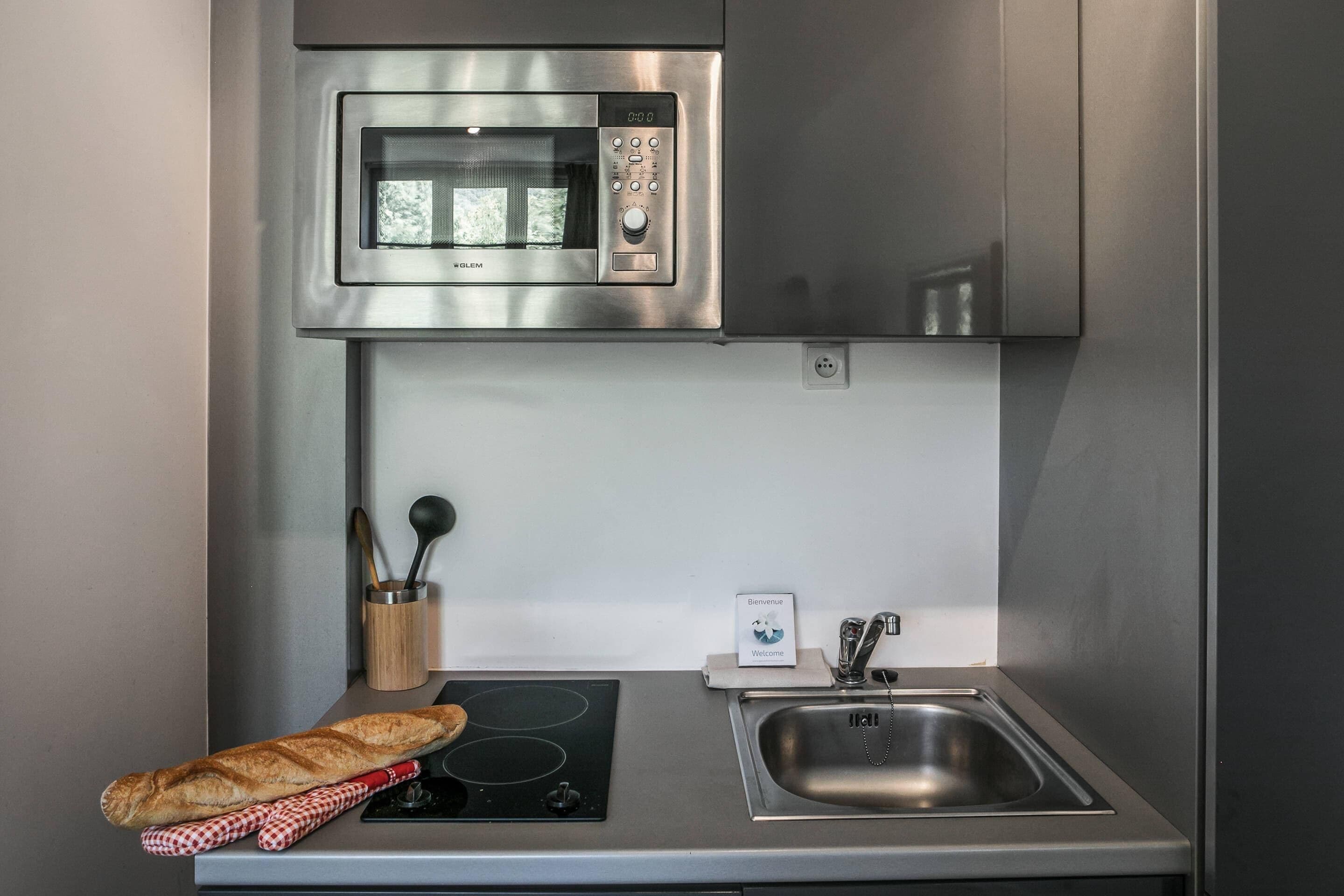 A compact kitchen with a built-in microwave, a stainless steel sink, and a small induction cooktop.