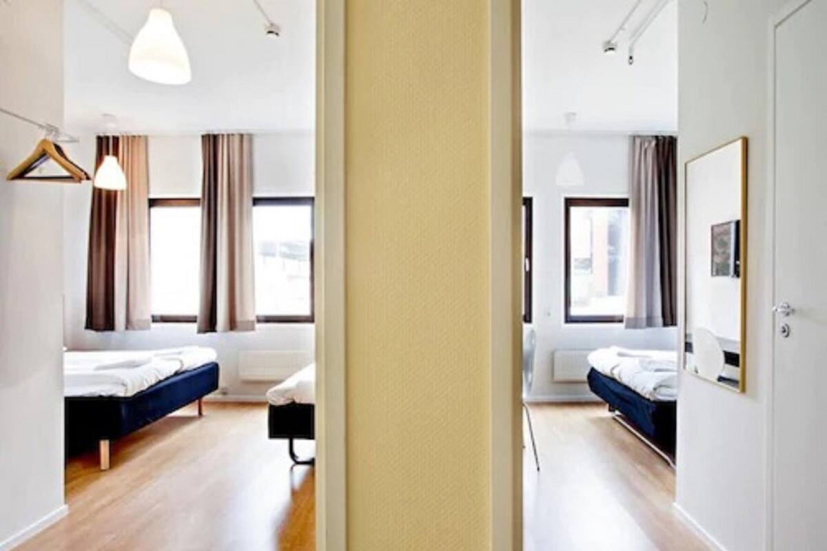 Ein modernes Hotelzimmer mit zwei Betten, einem großen Fenster und einem Spiegel.