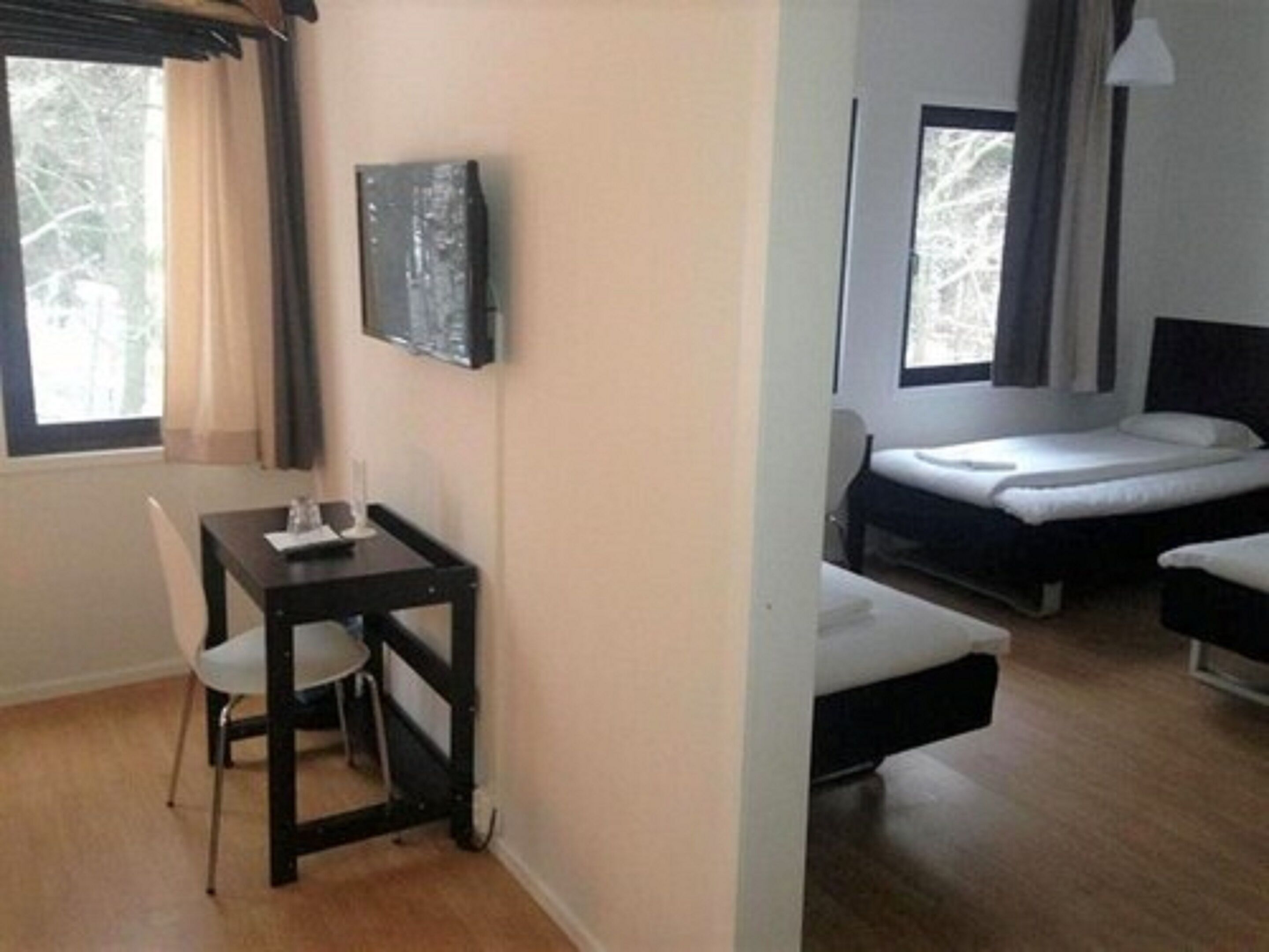 A small, compact room with a single bed, a desk, and a chair. There is a window providing natural light and a view of trees outside.
