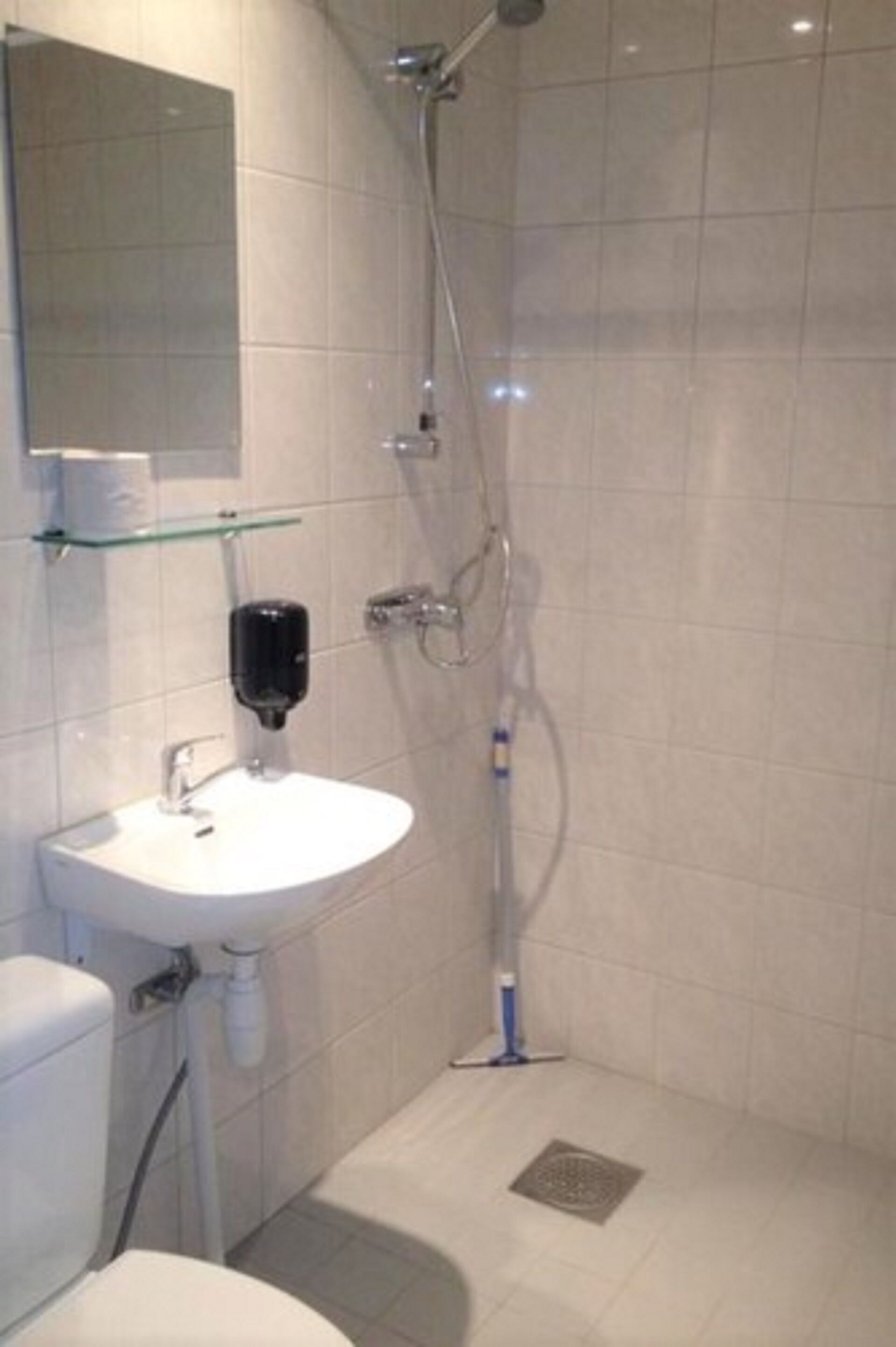 Een moderne badkamer met een wit wastafelmeubel, een glazen plank, een toilet en een douche.