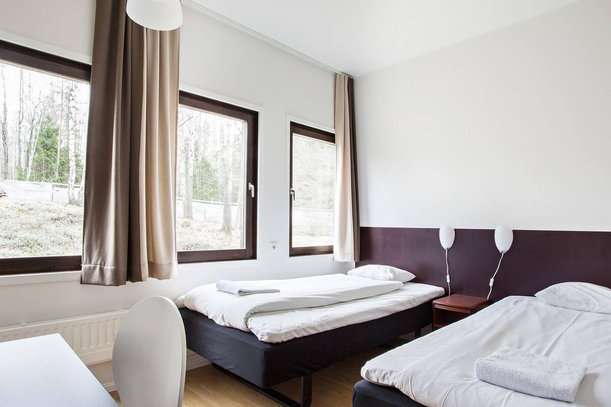 Ein Hotelzimmer mit zwei Betten, einem Schreibtisch und großen Fenstern mit Vorhängen.
