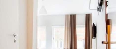 Una habitación moderna y bien iluminada con suelo de madera, una cama, un escritorio y una silla.