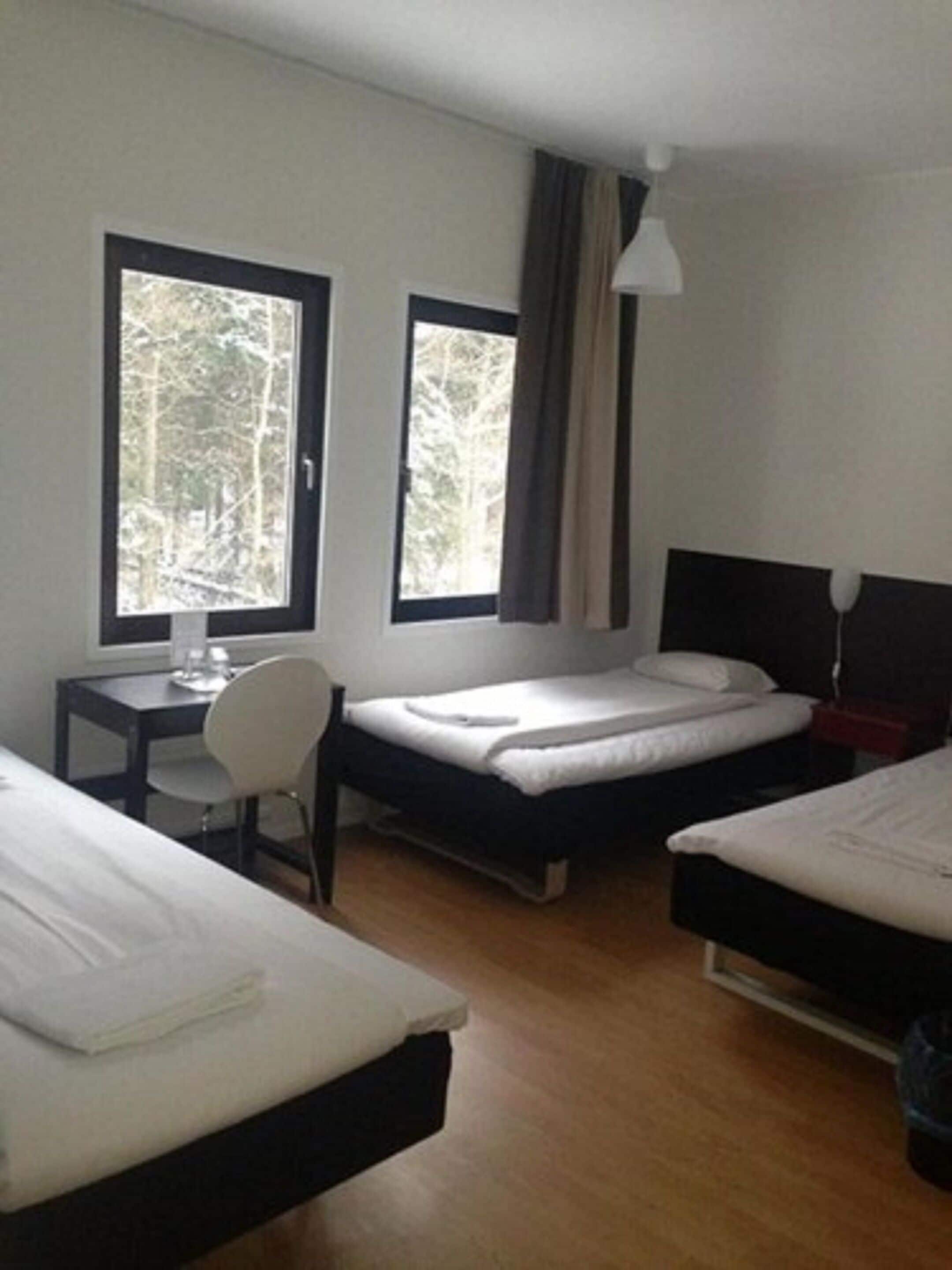A hotel room with two single beds, a desk with a chair, a window, and a lamp.