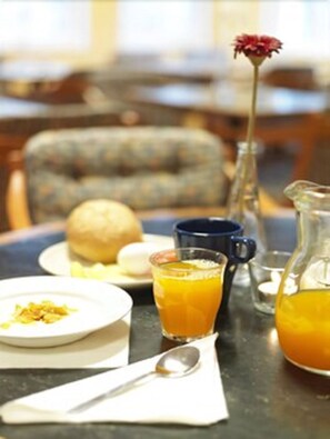 Ein Frühstückstisch mit einem Teller Essen, einem Glas Orangensaft, einer Saftkanne, einer Tasse und einem Löffel.
