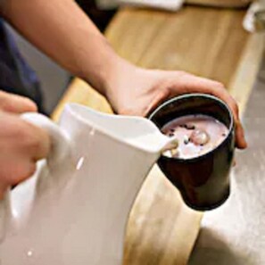 Eine Person gießt ein Getränk aus einer Kanne in eine Tasse.