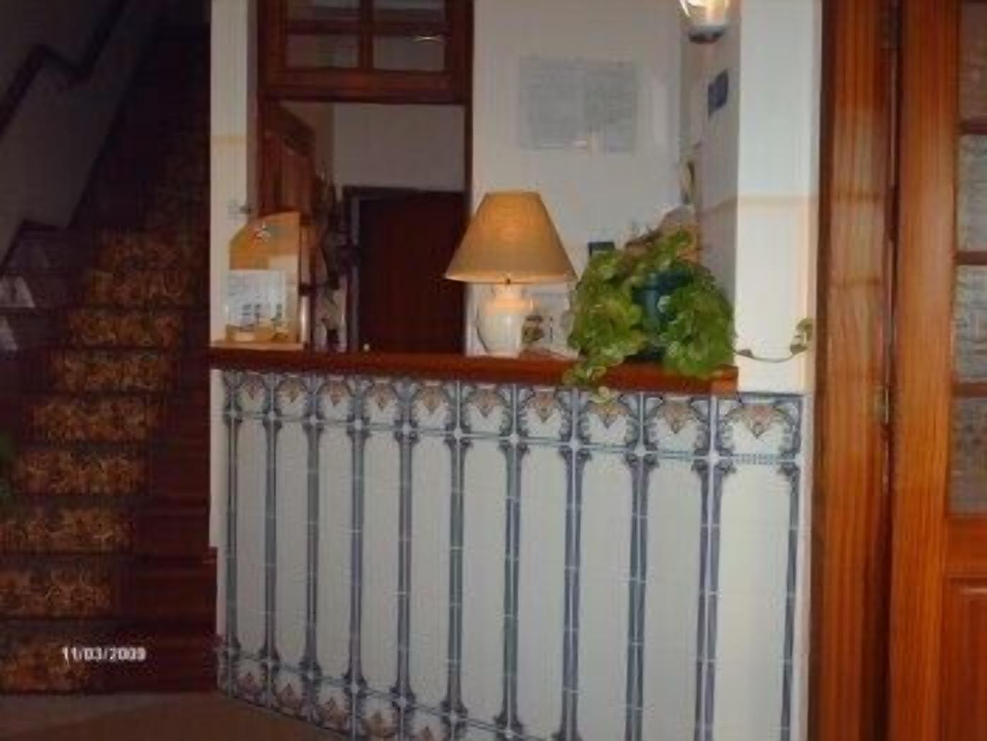 A staircase with a patterned railing, a wooden counter with a lamp, and a wall with a decorative tile border.