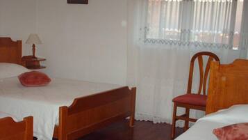 Quarto com cama de madeira, uma cadeira, mesa de cabeceira com abajur e janela com cortinas leves.
