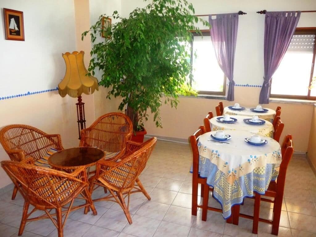 A dining area with wicker chairs and a round table, a potted plant, and a window with purple curtains.