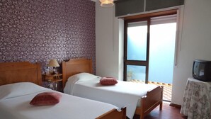 A room with two wooden beds, a small table with a television, and a window with a view of the sea.