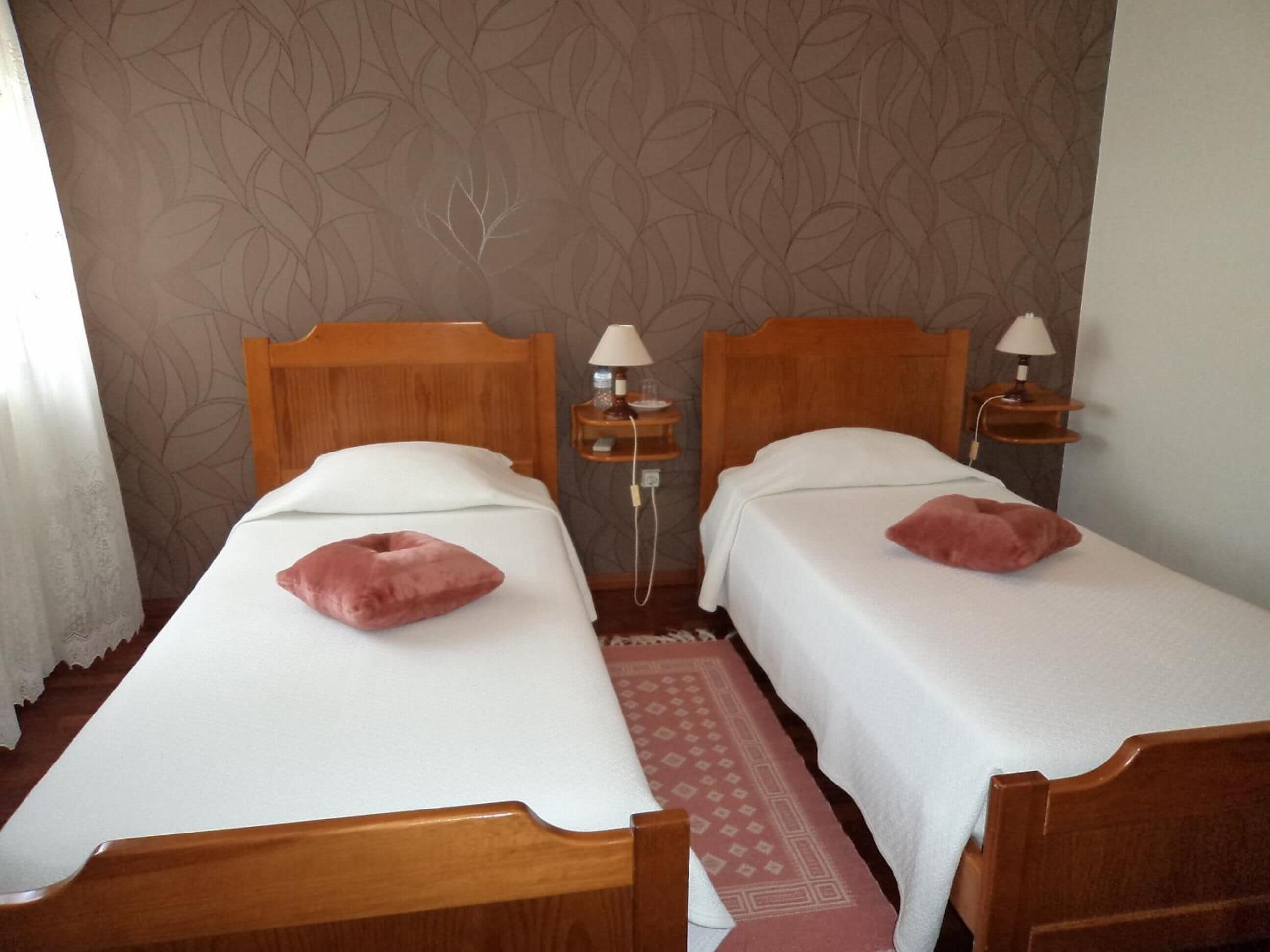 A hotel room with two wooden beds, white linens, and matching pillows. There are bedside tables with lamps and a patterned wall.
