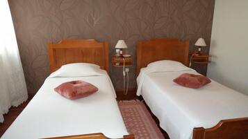 A hotel room with two wooden beds, white linens, and matching pillows. There are bedside tables with lamps and a patterned wall.
