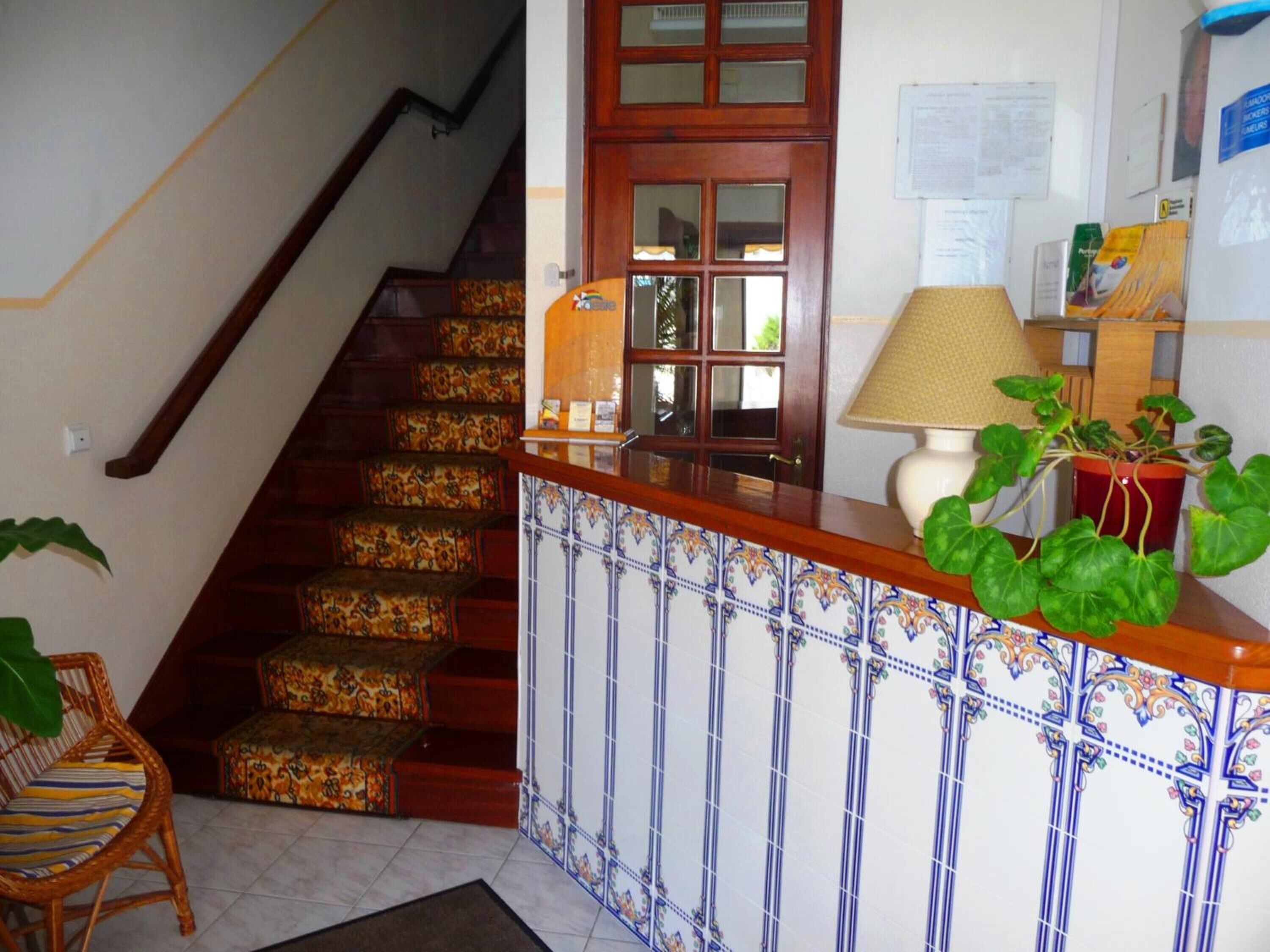 Una escalera con alfombra estampada, barandilla de madera y pared de azulejos con un borde decorativo.