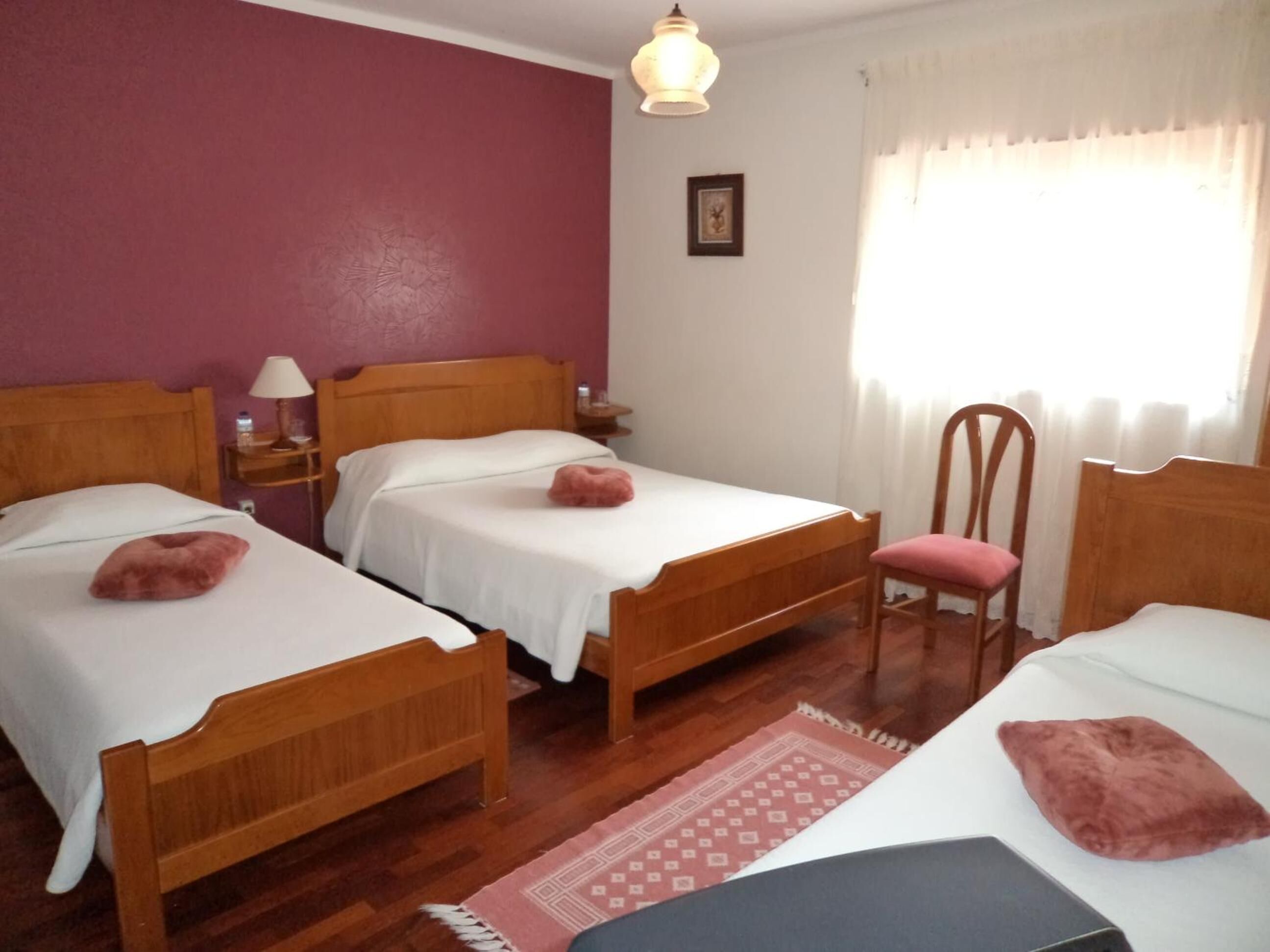 A room with two wooden beds, a chair, a nightstand, a lamp, and a window with curtains.