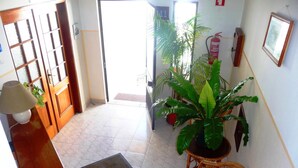 A hotel reception area with a wooden desk, a lamp, a potted plant, and a wicker chair.
