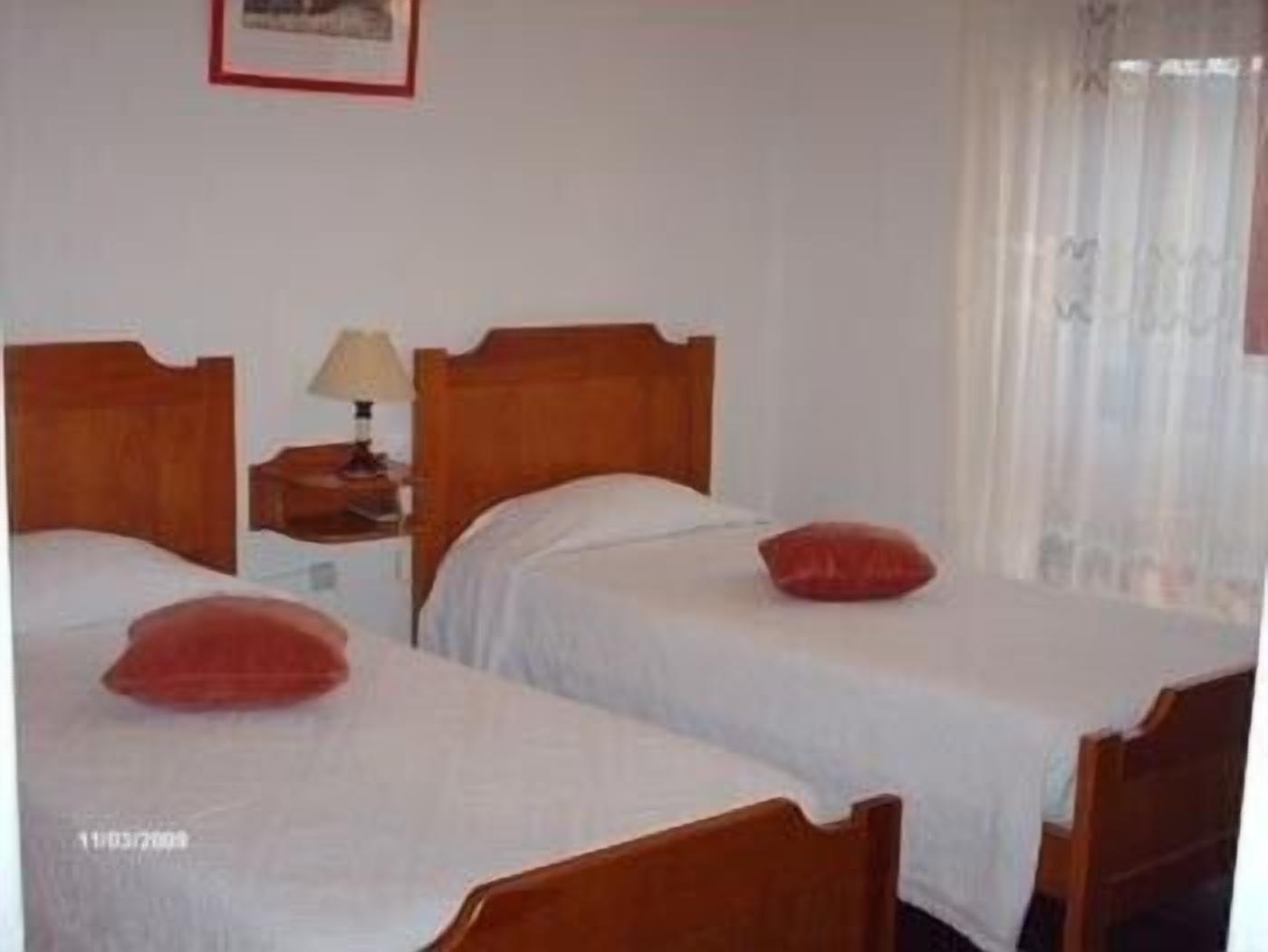 A hotel room with two single beds, a nightstand with a lamp, and a window with curtains.