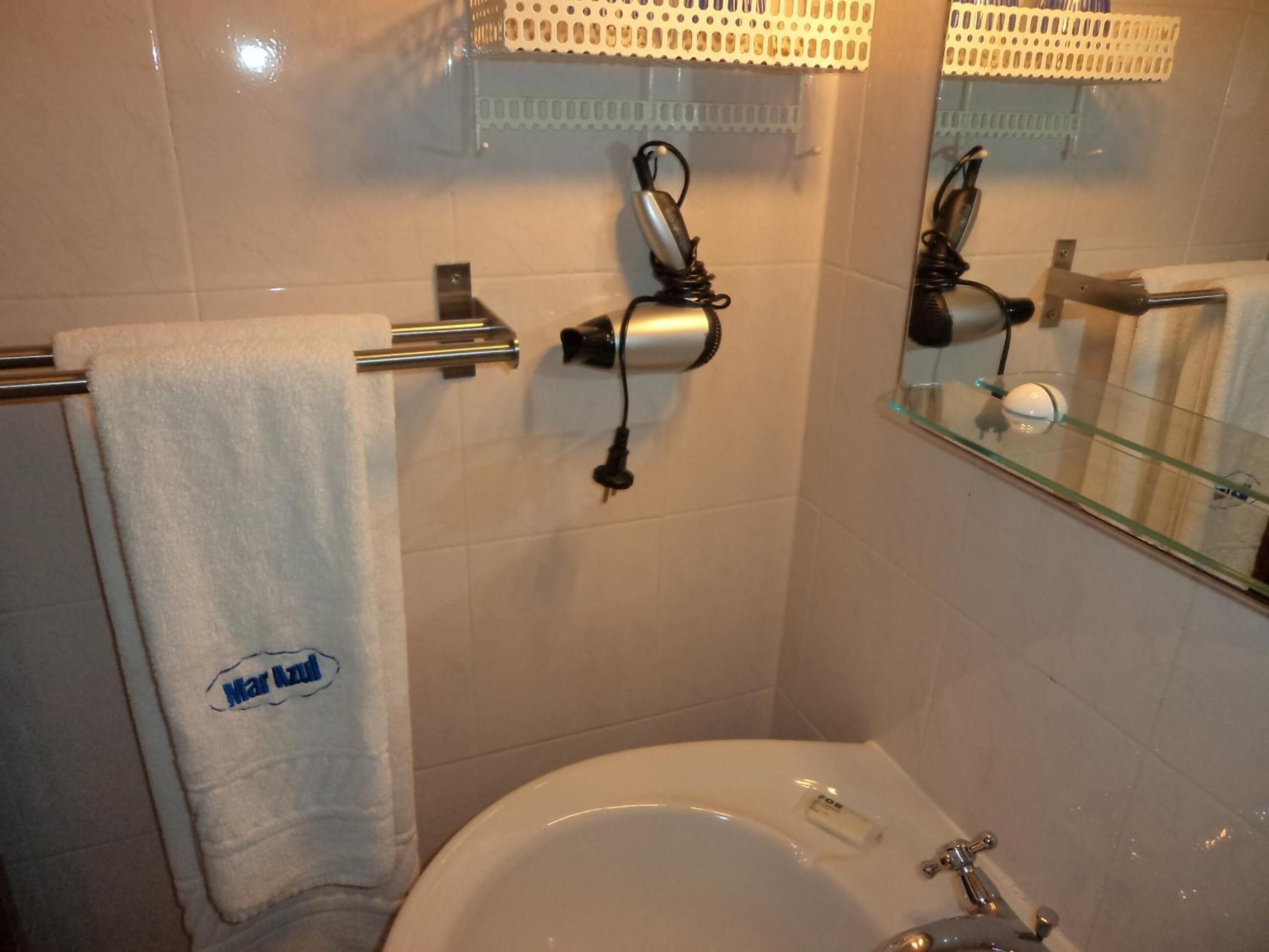 A bathroom with a white sink, a towel rack with a towel, and a hairdryer mounted on the wall.