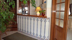 A reception area with a tiled wall, a wooden reception desk, a lamp, and a potted plant.