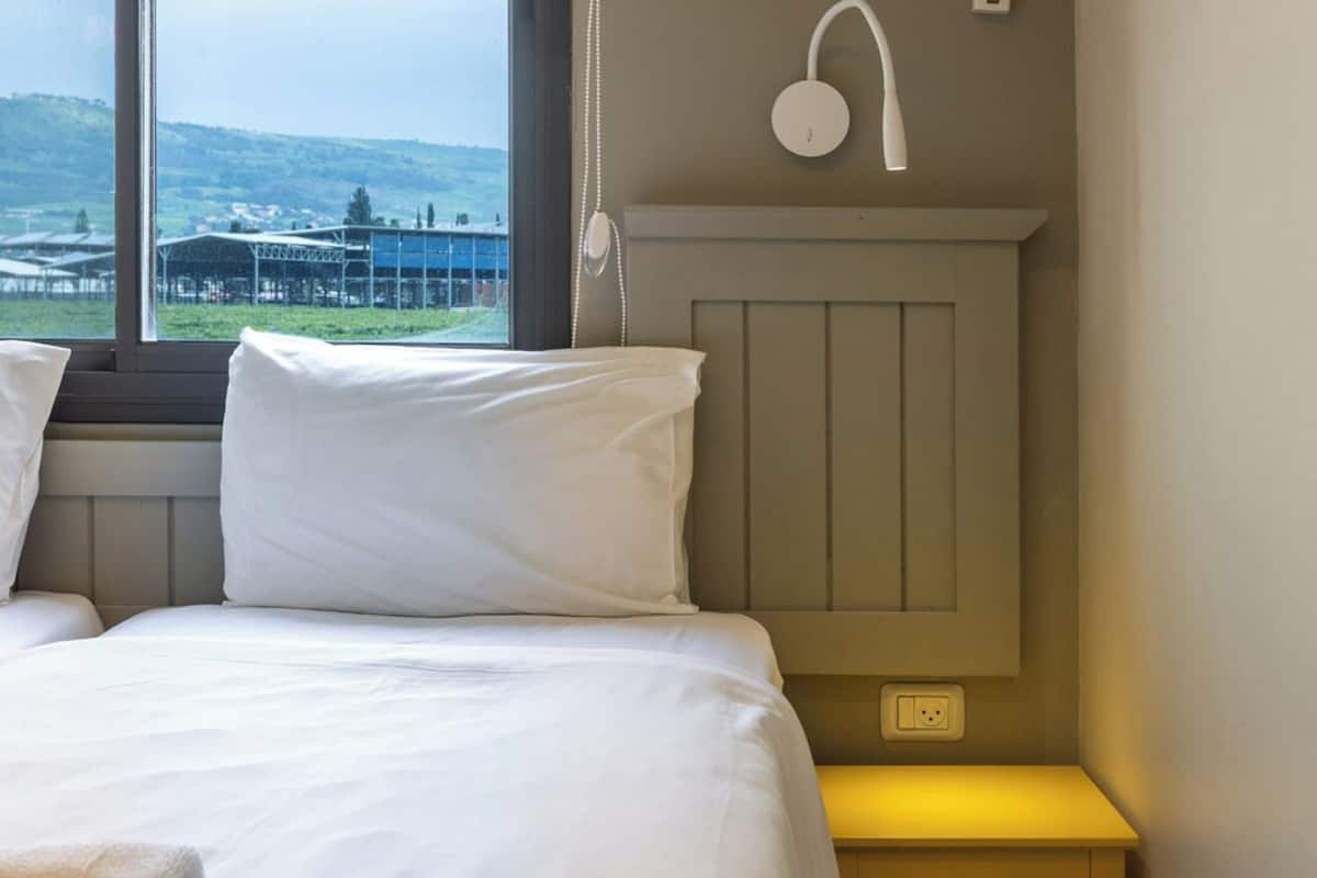 Ein Schlafzimmer mit Bett, Nachttisch, Wandlampe und Fenster mit Landschaftsblick.