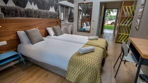 Habitación de hotel con dos camas, cabecera de madera, espejo, escritorio y vistas al exterior.