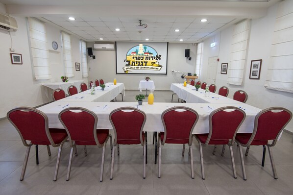 Un salón de conferencias con una larga mesa, sillas rojas y una pantalla para proyector.