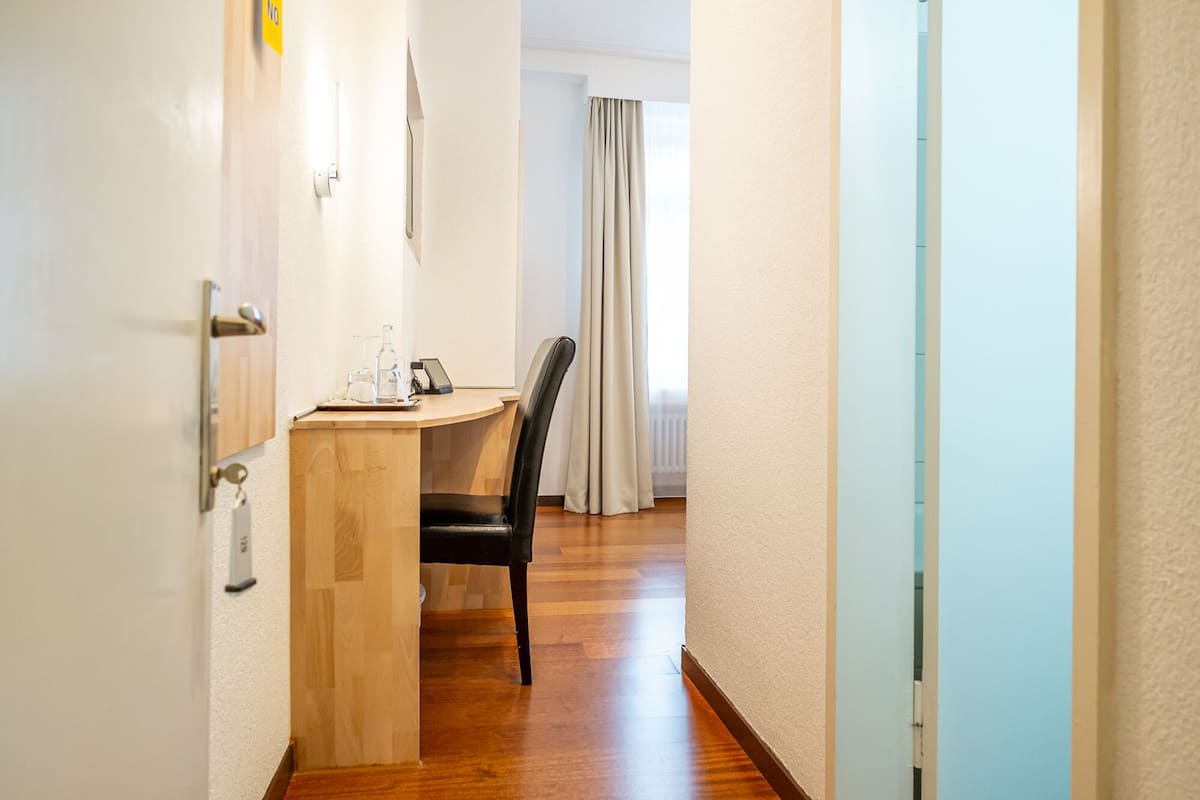 A hallway leading to a room with a wooden desk, a chair, and a window with curtains.