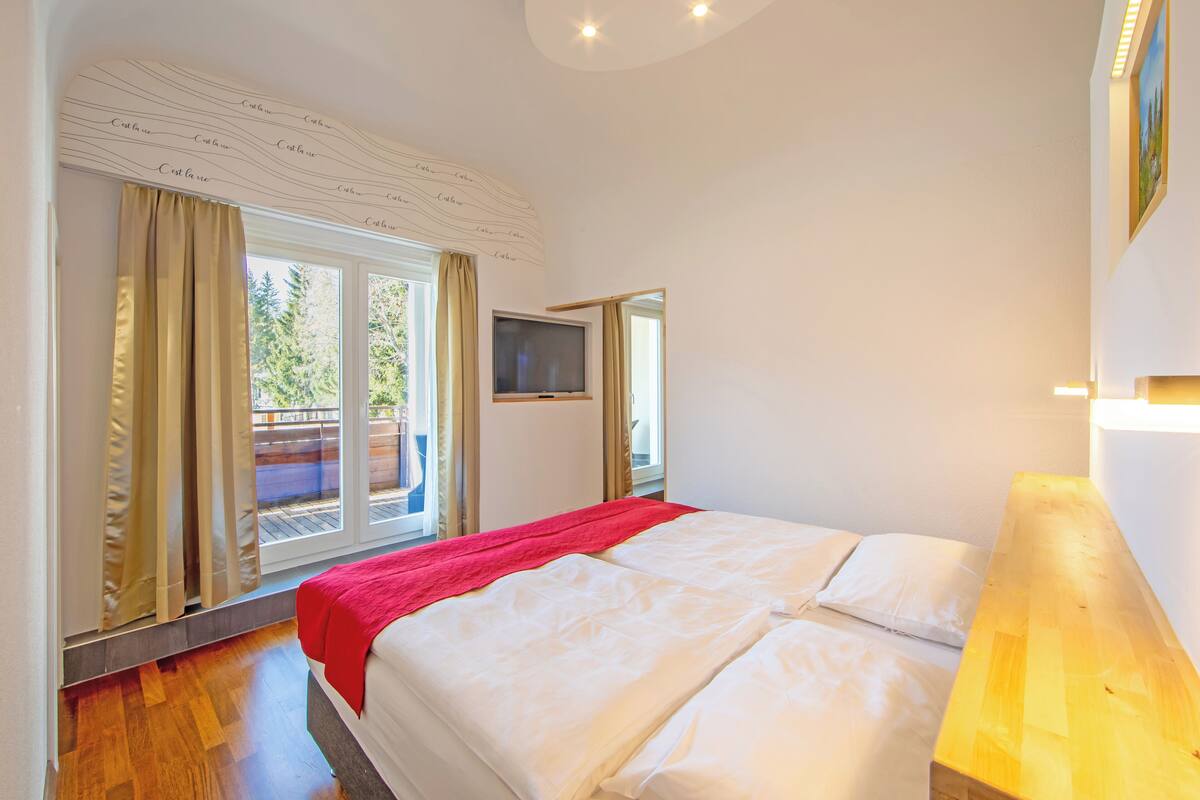 A hotel room with a large bed, a TV, and a balcony with curtains.