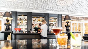 A bar area with a bartender preparing drinks, shelves stocked with bottles, and a modern ceiling design. - Hotel Europe Davos (Davos)