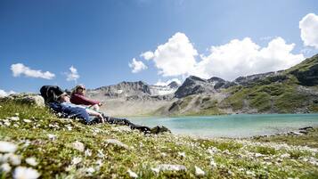 Una pareja relajándose en un césped con un lago y montañas al fondo.