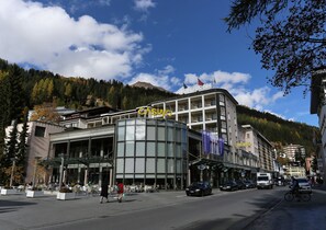 A modern hotel with a glass facade, outdoor seating, and flags indicating multiple brands. - Hotel Europe Davos (Davos)