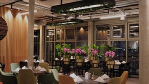 A modern restaurant with tables and chairs, potted plants, and large windows. - Hotel Europe Davos (Davos)