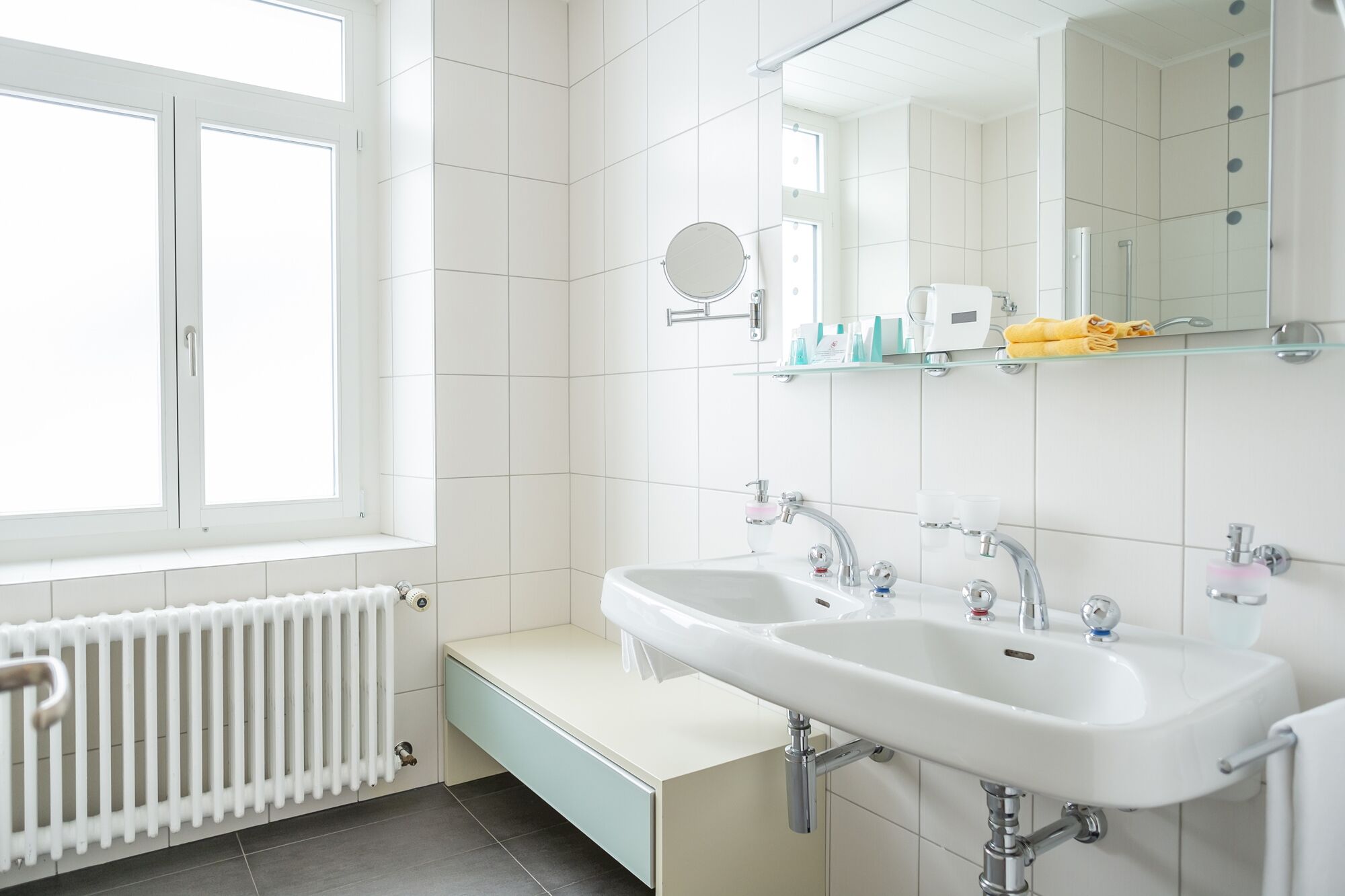 A modern bathroom with two sinks, a large mirror, and a window.