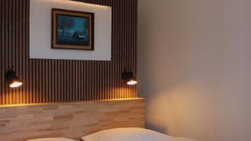 A modern bedroom with a wooden headboard, a framed picture, two bedside lamps, and a bed with white linens and a striped throw blanket.