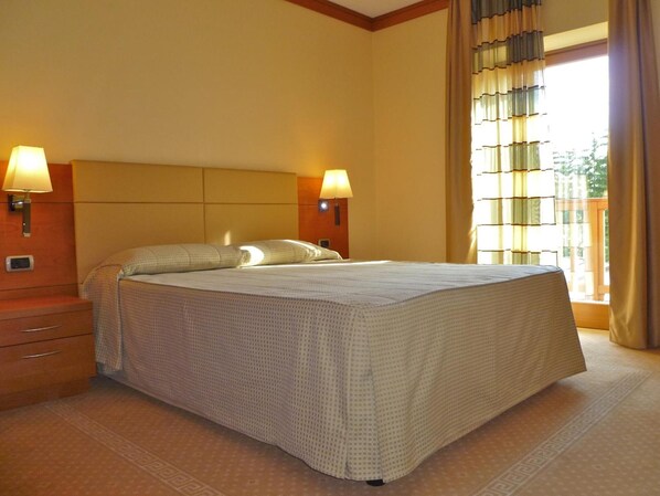 A hotel room with a large bed, two bedside lamps, a nightstand, and a window with curtains.