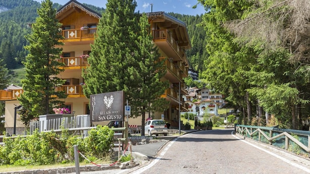 A hotel with a sign reading "HOTEL REIIS SAN GIUSTO" surrounded by trees and mountains. - Relais San Giusto (Campitello di Fassa)