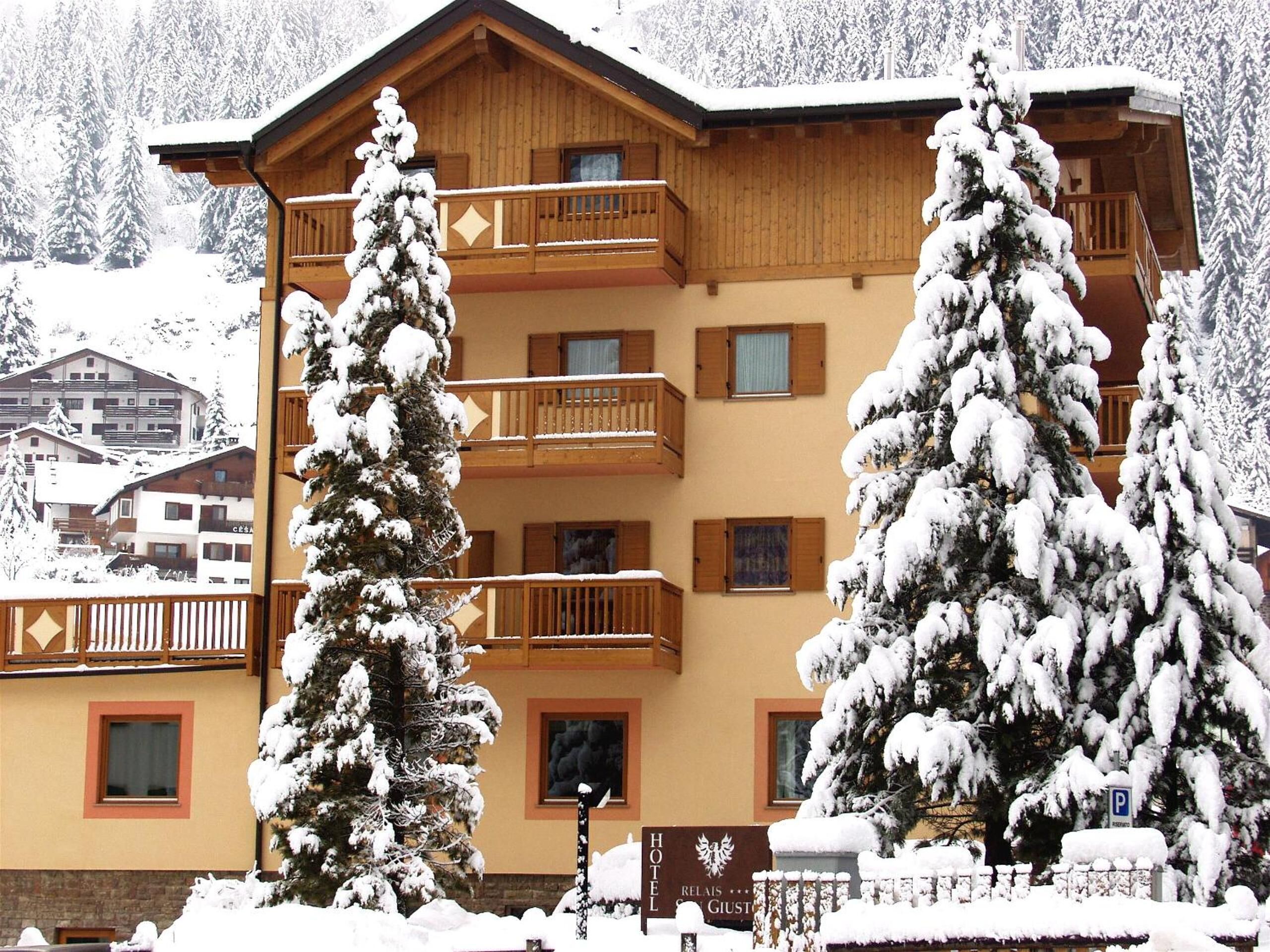 A hotel with a wooden facade, balconies, and snow-covered trees.