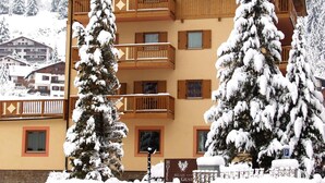 A hotel with a wooden facade, balconies, and snow-covered trees. - Relais San Giusto (Campitello di Fassa)