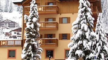 A hotel with a wooden facade, balconies, and snow-covered trees.