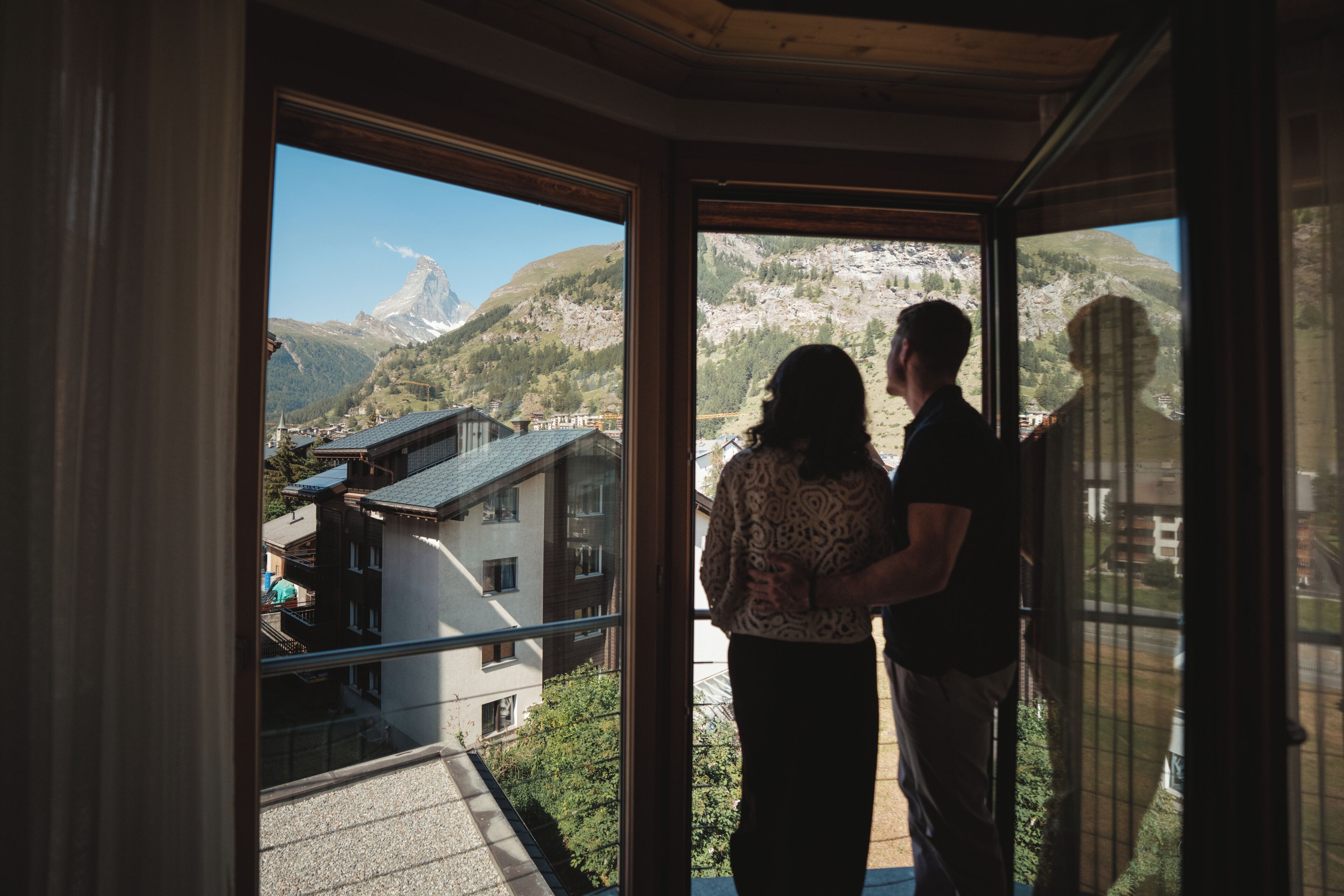 Una pareja de pie junto a una ventana con vistas a un paisaje montañoso.