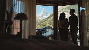 A room with a bed, a lamp, and a view of a mountain.