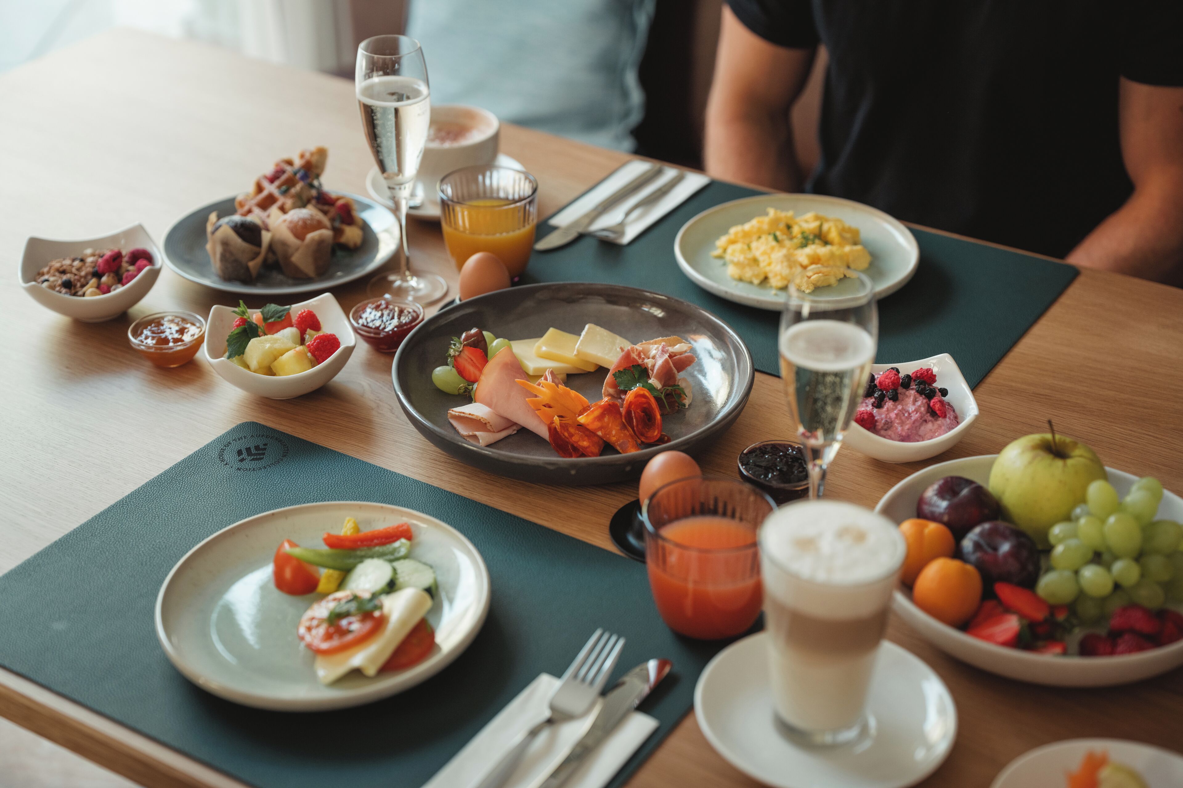 A breakfast setting with various dishes, including fruits, eggs, and pastries, on a wooden table.