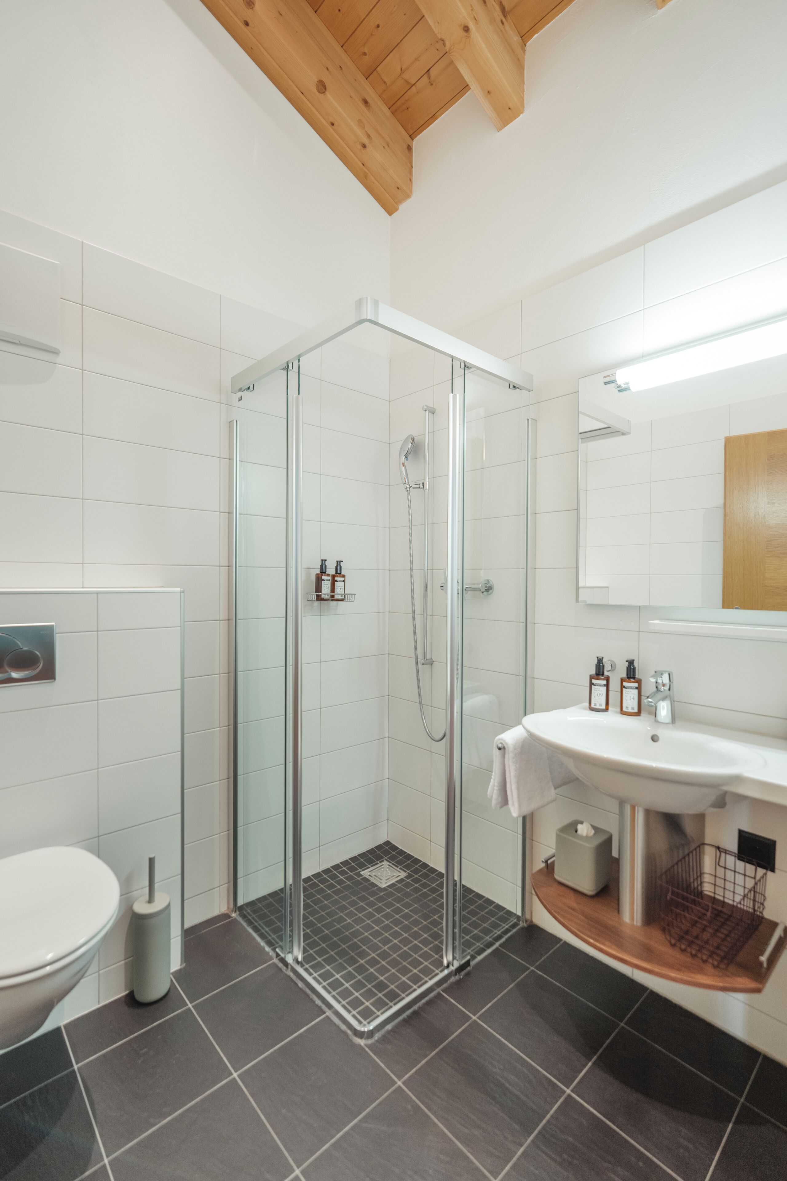 Un baño moderno con cabina de ducha de vidrio, un lavabo blanco y techo de madera.