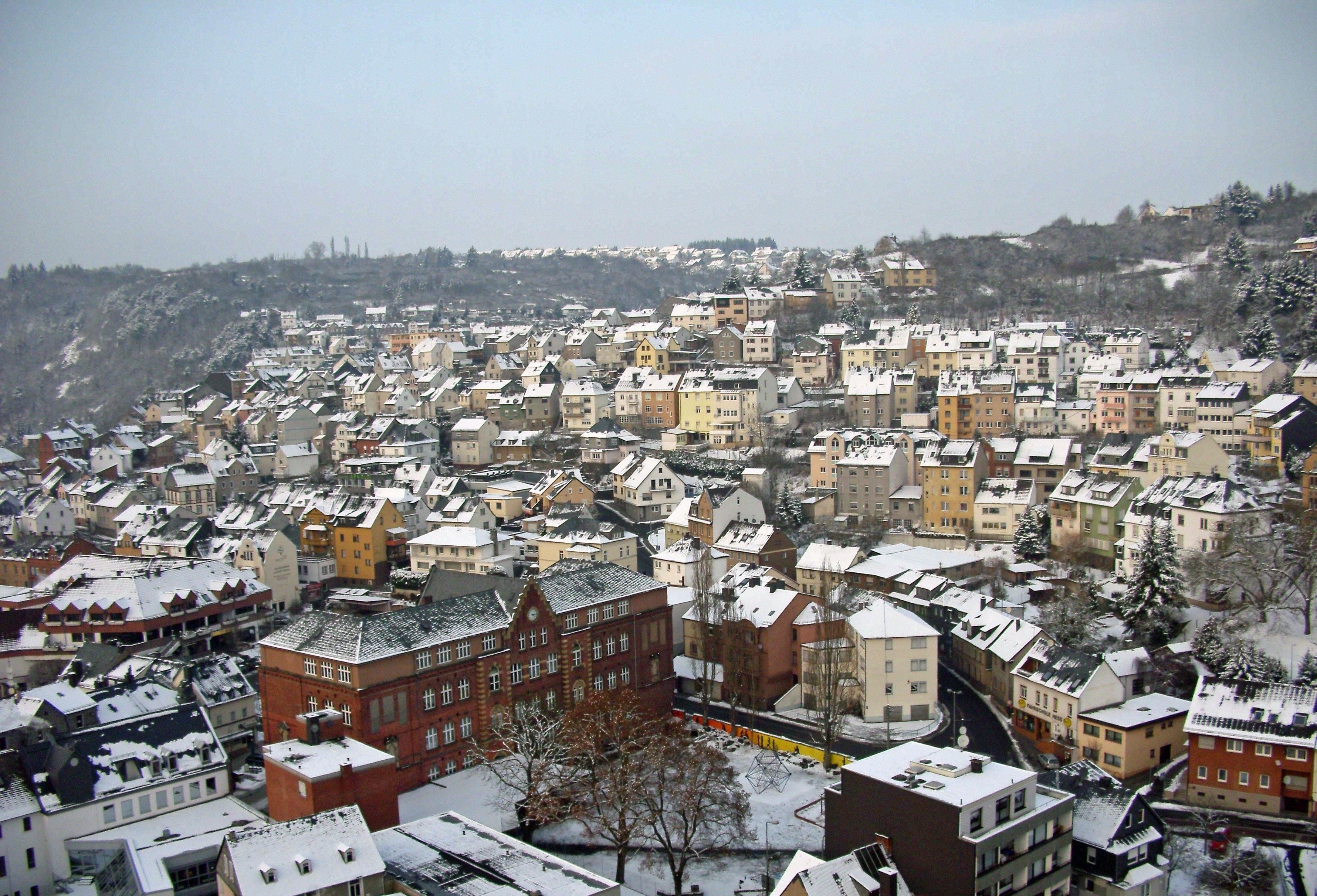 A densely packed urban area with snow-covered buildings and a hilly backdrop.
