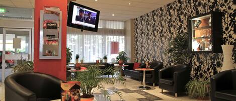 A hotel lobby with black leather sofas, a TV mounted on the wall, and a patterned wallpaper.