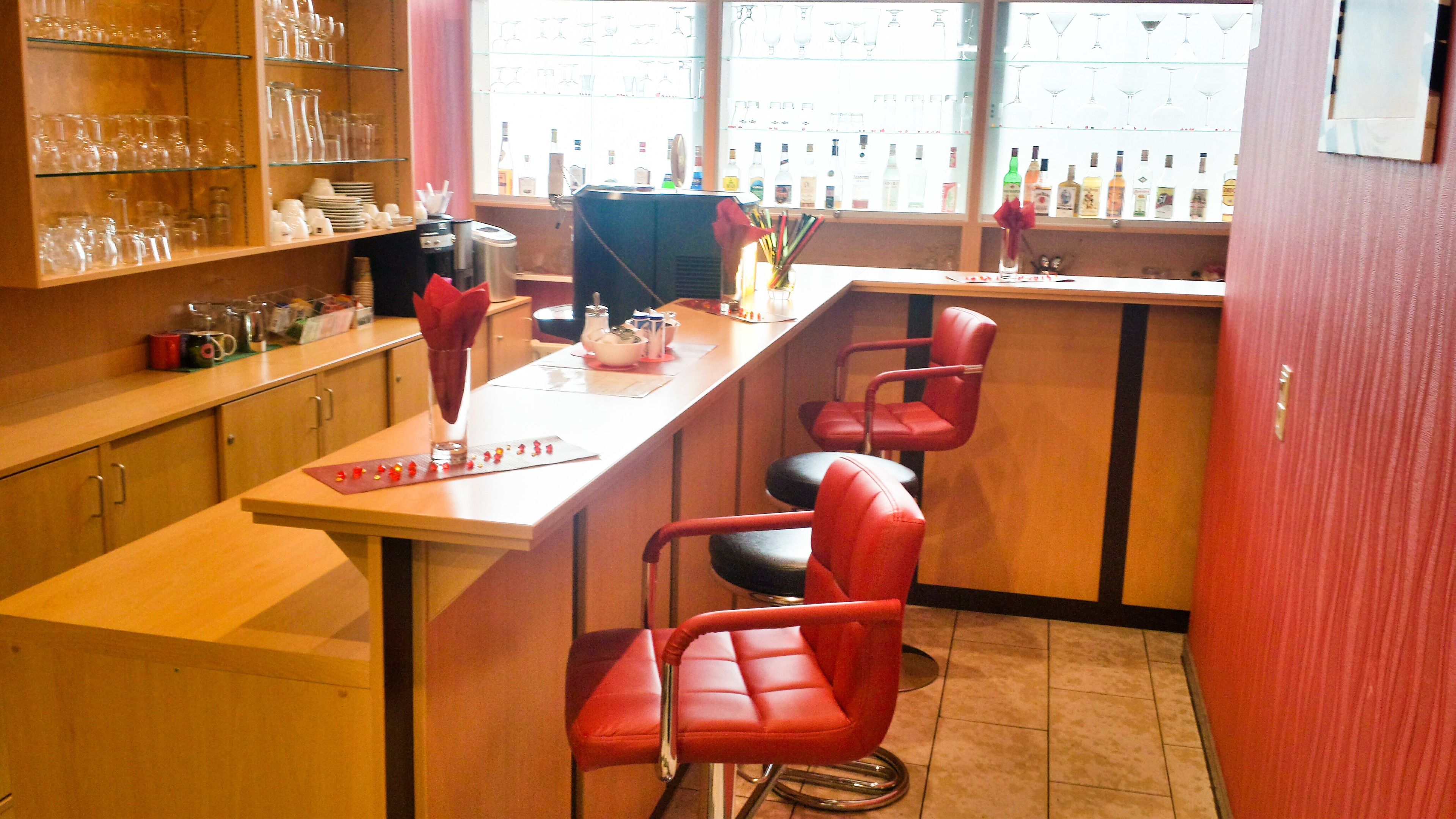 A bar area with a counter, bar stools, and shelves with glasses and bottles.