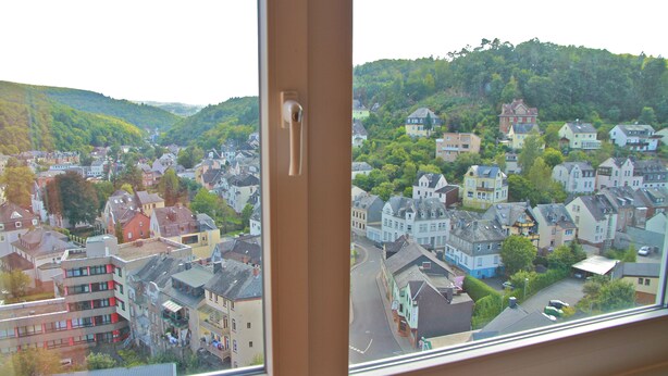 Vista da janela sobre uma cidade, com vários edifícios, uma rua e uma colina ao fundo.