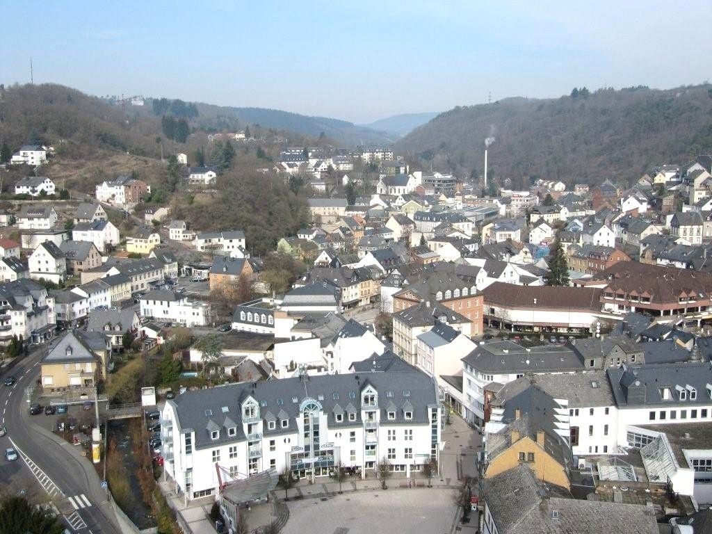 A town with a central square, surrounded by buildings, including a prominent hotel with a large entrance and a clock tower.