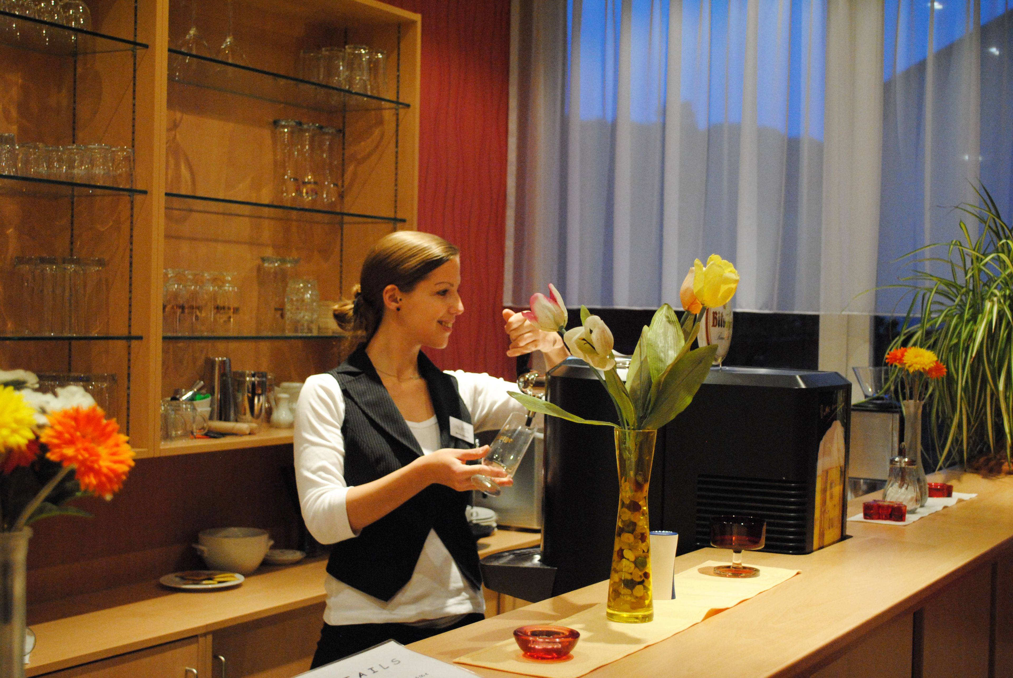 A woman at a bar counter with a vase of flowers, a glass, and a menu.