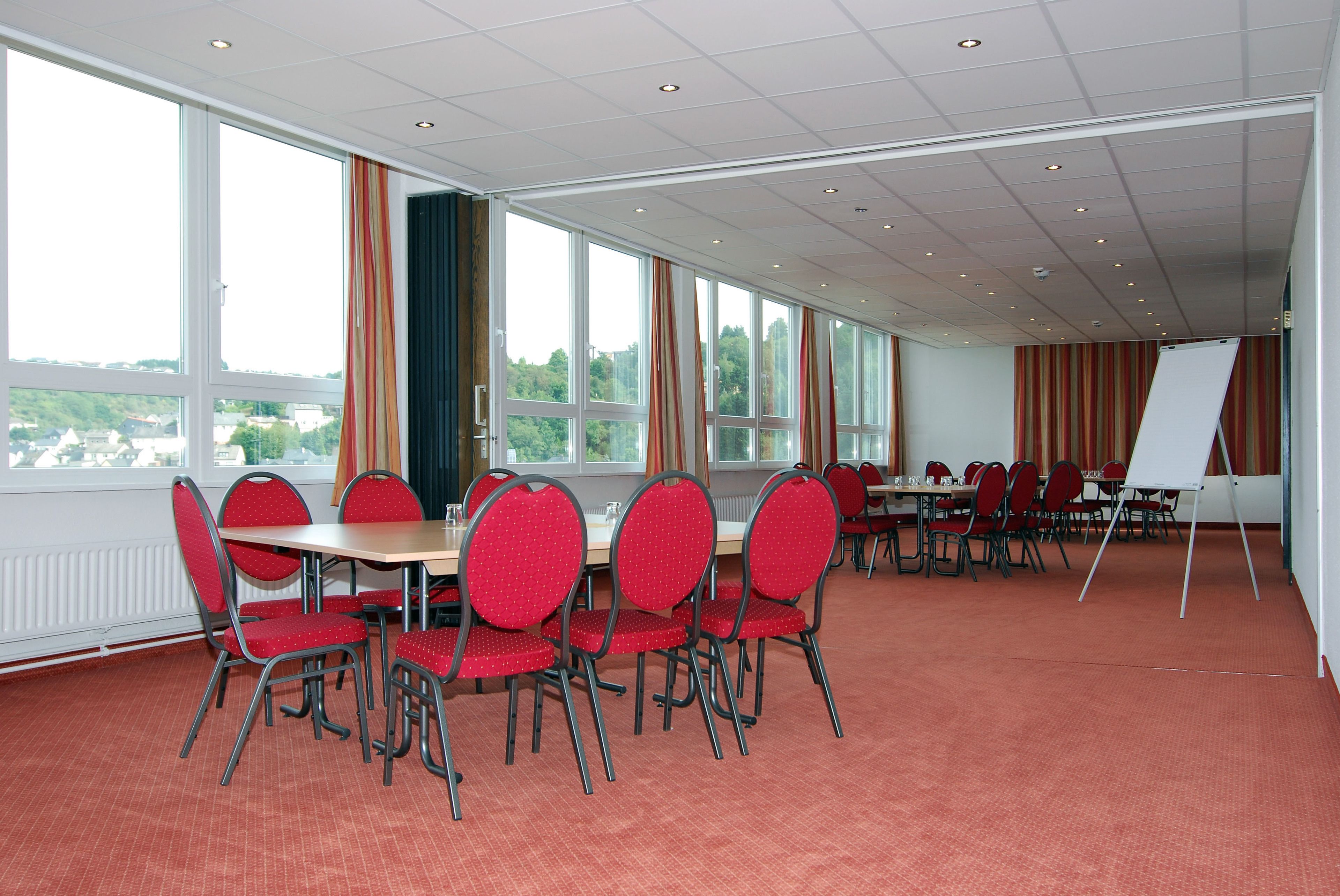 A conference room with red chairs and tables, large windows, and a whiteboard.