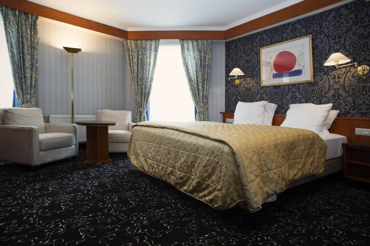 A hotel room with a large bed, two armchairs, a floor lamp, and a painting on the wall.